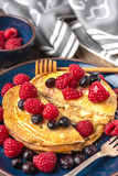 Sweet homemade pancakes with raspberries and blueberries on blue plate.