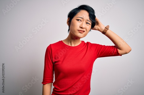 Young beautiful asian girl wearing casual red t-shirt standing over isolated white background confuse and wondering about question. Uncertain with doubt, thinking with hand on head. Pensive concept.