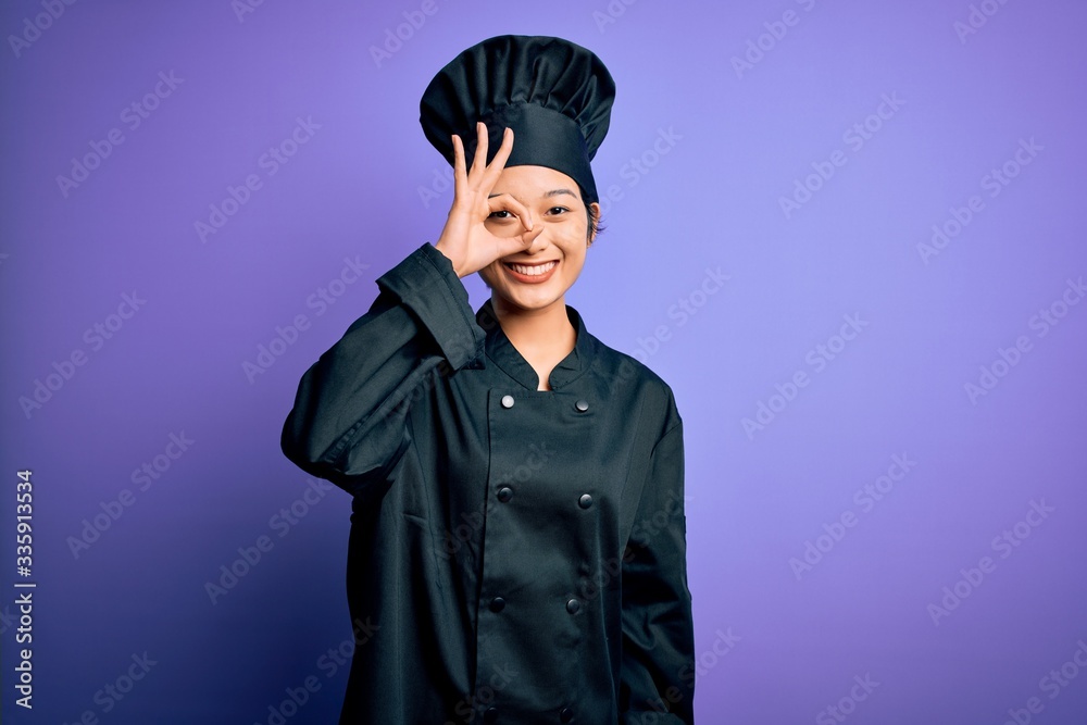 Young beautiful chinese chef woman wearing cooker uniform and hat over purple background doing ok gesture with hand smiling, eye looking through fingers with happy face. Young beautiful chinese chef woman wearing cooker uniform and hat over purple background doing ok gesture with hand smiling, eye looking through fingers with happy face.