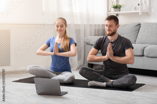 Young millennial couple practicing yoga with instructor online