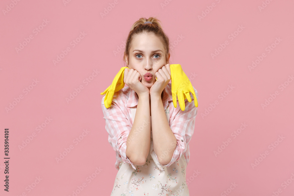 Pretty young woman housewife in casual clothes, apron doing housework isolated on pastel pink wall background studio portrait. Housekeeping concept. Hold rubber gloves, put hands on blowing cheeks. Pretty young woman housewife in casual clothes, apron doing housework isolated on pastel pink wall background studio portrait. Housekeeping concept. Hold rubber gloves, put hands on blowing cheeks.