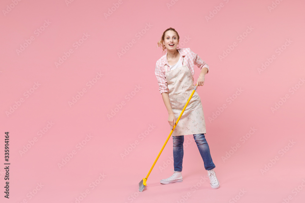 Cheerful funny young woman housewife in casual clothes, apron doing housework isolated on pastel pink wall background studio portrait. Housekeeping concept. Mock up copy space. Sweeping with broom. Cheerful funny young woman housewife in casual clothes, apron doing housework isolated on pastel pink wall background studio portrait. Housekeeping concept. Mock up copy space. Sweeping with broom.