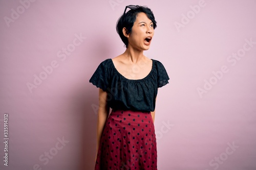 Young beautiful asian girl wearing casual dress standing over isolated pink background angry and mad screaming frustrated and furious, shouting with anger. Rage and aggressive concept.