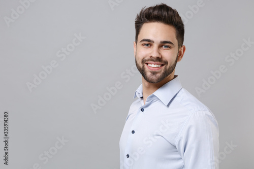 Side view of smiling young unshaven business man in light shirt posing isolated on grey wall background studio portrait. Achievement career wealth business concept. Mock up copy space. Looking camera. © ViDi Studio