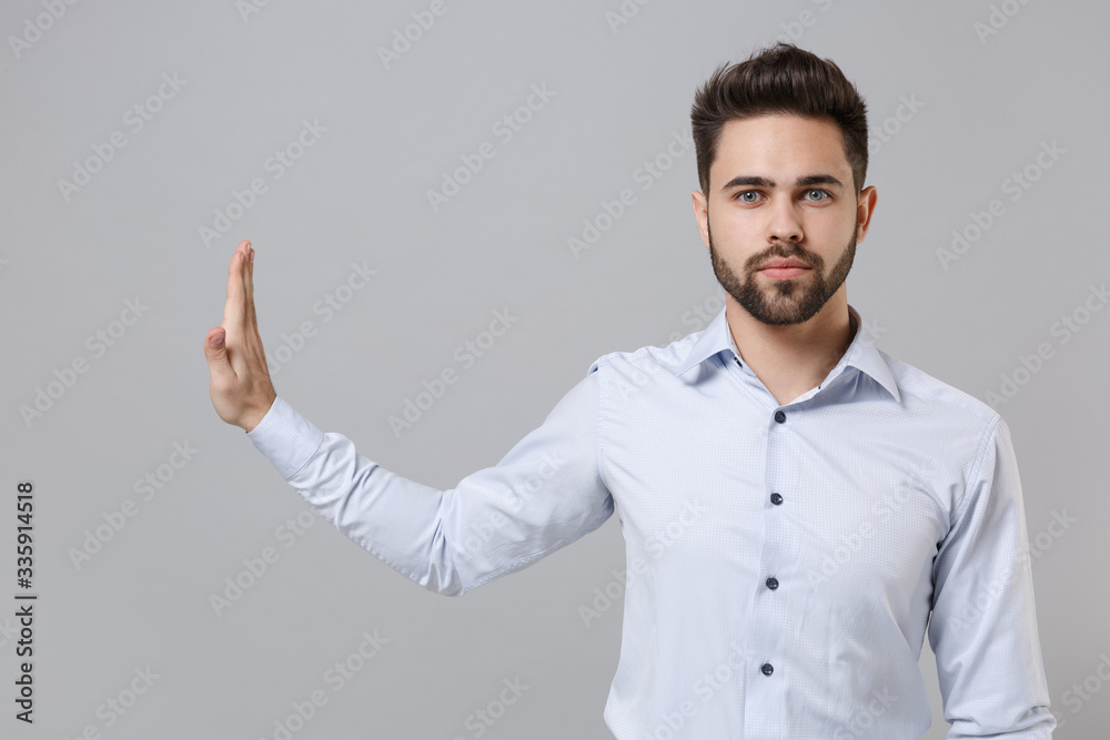 Serious young unshaven business man in light shirt posing isolated on grey background in studio. Achievement career wealth business concept. Mock up copy space. Showing stop gesture aside with palm. Serious young unshaven business man in light shirt posing isolated on grey background in studio. Achievement career wealth business concept. Mock up copy space. Showing stop gesture aside with palm.