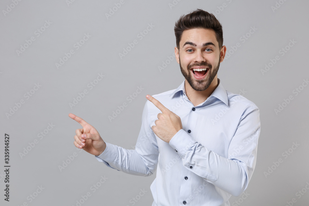 Excited young unshaven business man in light shirt posing isolated on grey background studio portrait. Achievement career wealth business concept. Mock up copy space. Pointing index fingers aside up. Excited young unshaven business man in light shirt posing isolated on grey background studio portrait. Achievement career wealth business concept. Mock up copy space. Pointing index fingers aside up.