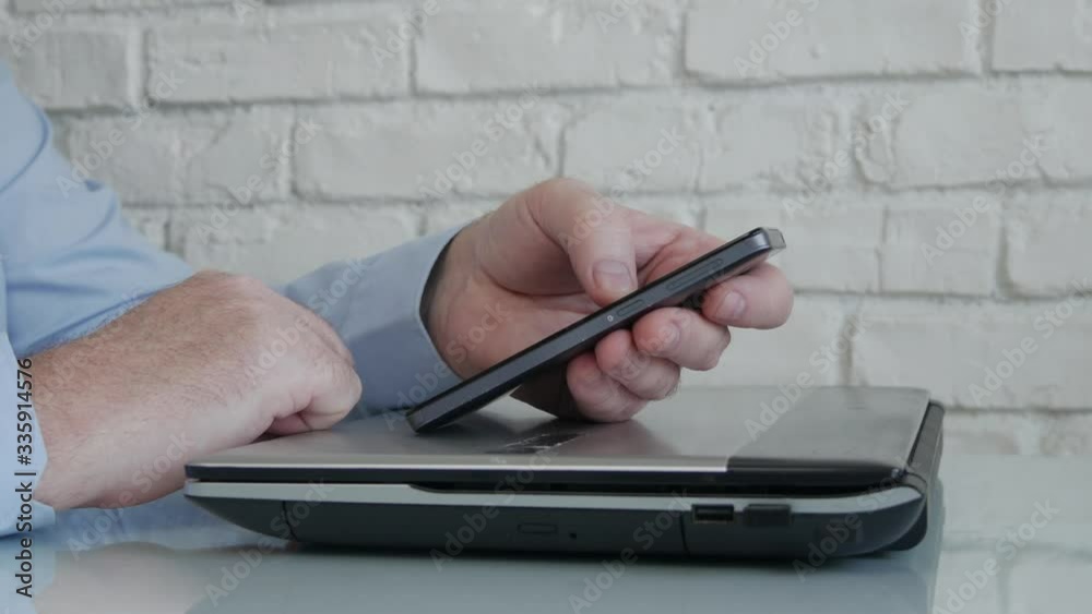 Businessman Using a Cellphone Texting and Working Online from Home, Man Accessing an Online Connection with Office from Phone and Laptop Businessman Using a Cellphone Texting and Working Online from Home, Man Accessing an Online Connection with Office from Phone and Laptop