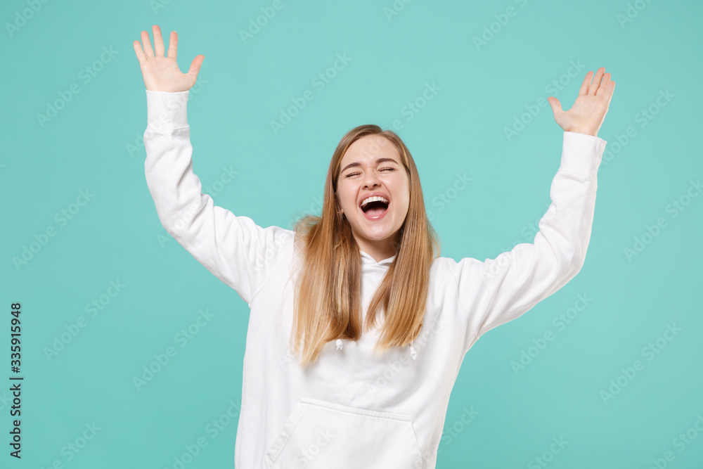Happy funny young woman girl in casual white hoodie posing isolated on blue turquoise background in studio. People lifestyle concept. Mock up copy space. Rising spreading hands, keeping eyes closed. Happy funny young woman girl in casual white hoodie posing isolated on blue turquoise background in studio. People lifestyle concept. Mock up copy space. Rising spreading hands, keeping eyes closed.