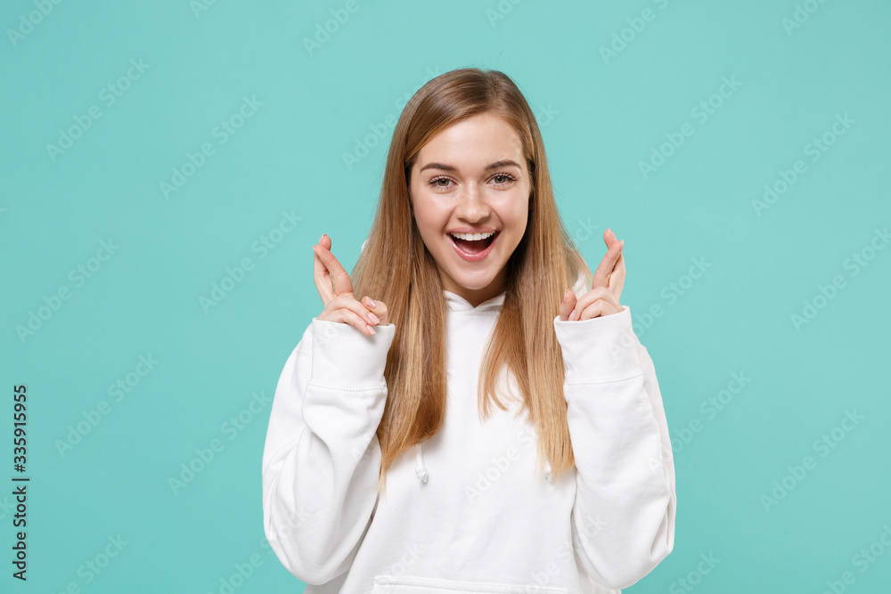 Cheerful young woman girl in casual white hoodie isolated on blue turquoise background. People lifestyle concept. Mock up copy space. Waiting for special moment keeping fingers crossed making wish. Cheerful young woman girl in casual white hoodie isolated on blue turquoise background. People lifestyle concept. Mock up copy space. Waiting for special moment keeping fingers crossed making wish.