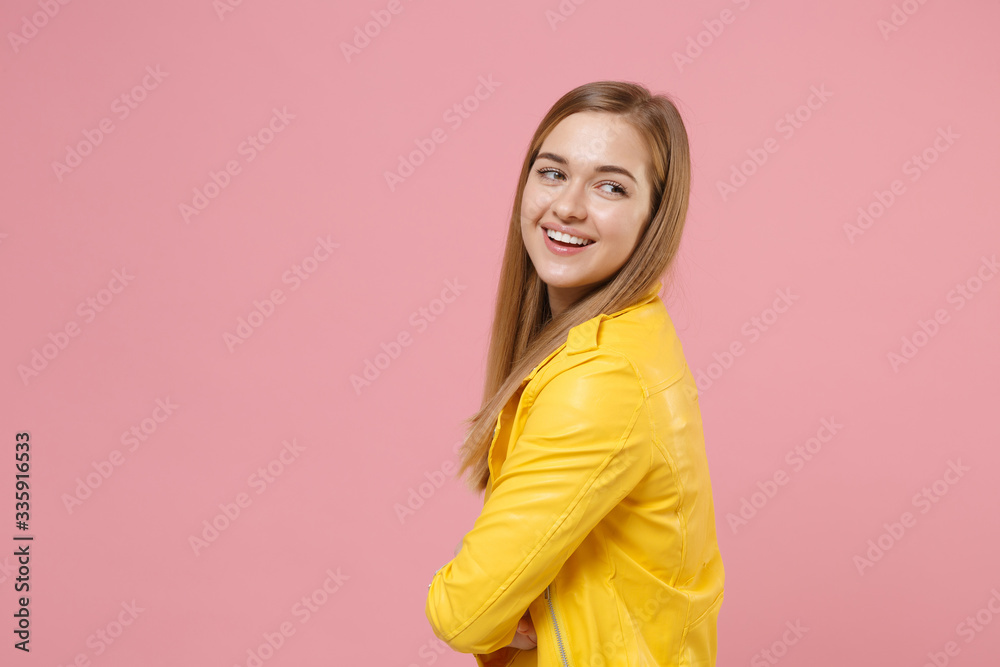 Side view of cheerful young woman girl in yellow leather jacket posing isolated on pastel pink background in studio. People lifestyle concept. Mock up copy space. Holding hands crossed, looking aside. Side view of cheerful young woman girl in yellow leather jacket posing isolated on pastel pink background in studio. People lifestyle concept. Mock up copy space. Holding hands crossed, looking aside.