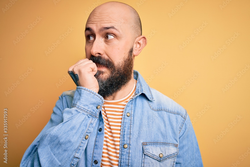 Handsome bald man with beard wearing casual denim jacket and striped t-shirt looking stressed and nervous with hands on mouth biting nails. Anxiety problem. Handsome bald man with beard wearing casual denim jacket and striped t-shirt looking stressed and nervous with hands on mouth biting nails. Anxiety problem.