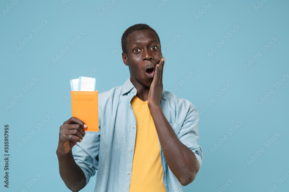 Shocked young african american man guy in casual shirt, yellow t-shirt isolated on blue background. People lifestyle concept. Mock up copy space. Hold passport ticket boarding pass put hand on cheek. Shocked young african american man guy in casual shirt, yellow t-shirt isolated on blue background. People lifestyle concept. Mock up copy space. Hold passport ticket boarding pass put hand on cheek.