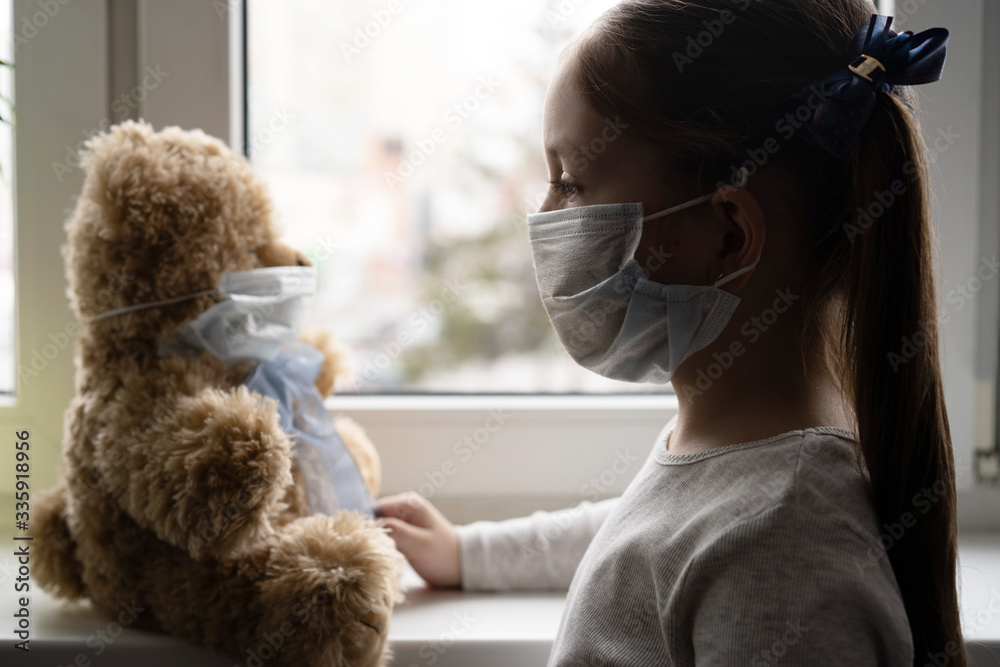 Sad child and his teddy bear both in protective medical masks. Children and illness COVID-2019 disease concept