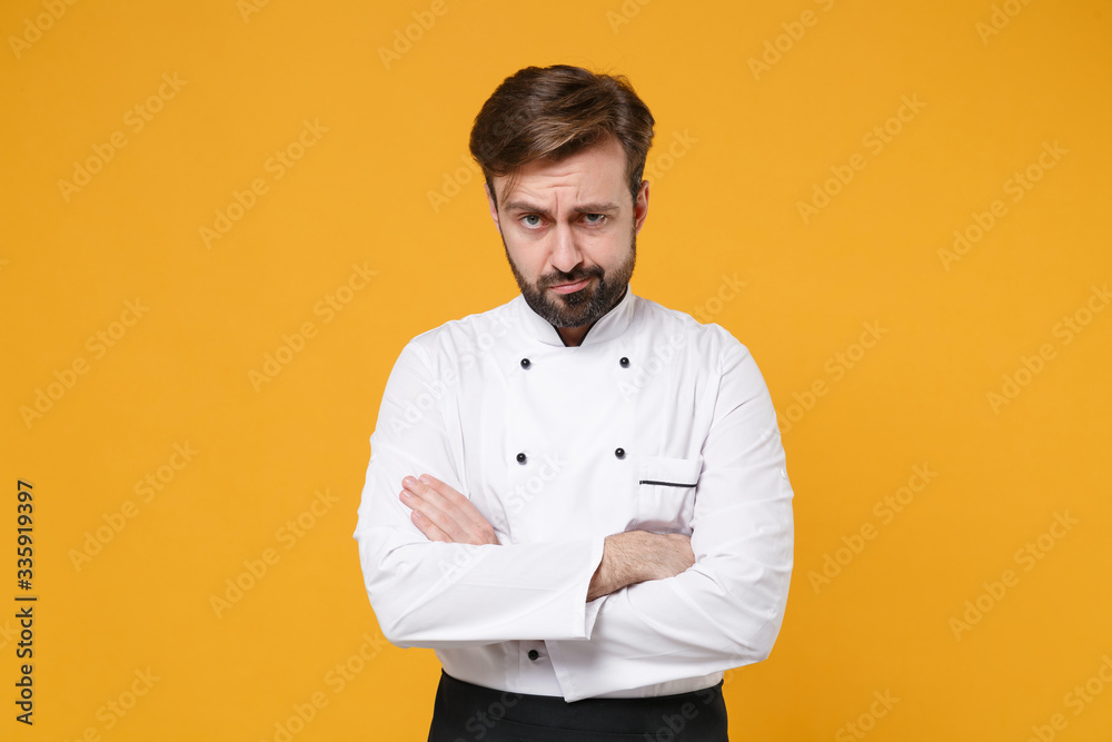 Perplexed confused young bearded male chef cook or baker man in white uniform shirt posing isolated on yellow background in studio. Cooking food concept. Mock up copy space. Holding hands crossed. Perplexed confused young bearded male chef cook or baker man in white uniform shirt posing isolated on yellow background in studio. Cooking food concept. Mock up copy space. Holding hands crossed.