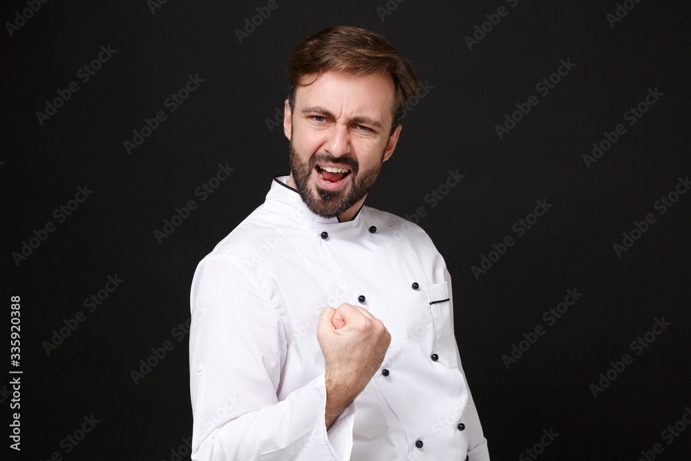 Excited young bearded male chef cook or baker man in white uniform shirt posing isolated on black wall background studio portrait. Cooking food concept. Mock up copy space. Doing winner gesture. Excited young bearded male chef cook or baker man in white uniform shirt posing isolated on black wall background studio portrait. Cooking food concept. Mock up copy space. Doing winner gesture.