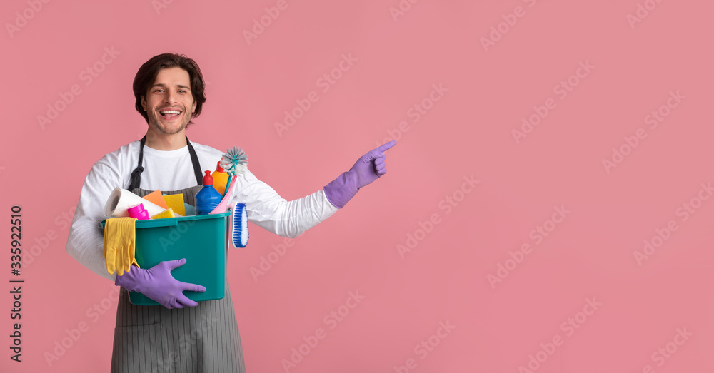 Cheerful Janitor Man Holding Basket With Cleaning Supplies And Pointing Aside Cheerful Janitor Man Holding Basket With Cleaning Supplies And Pointing Aside