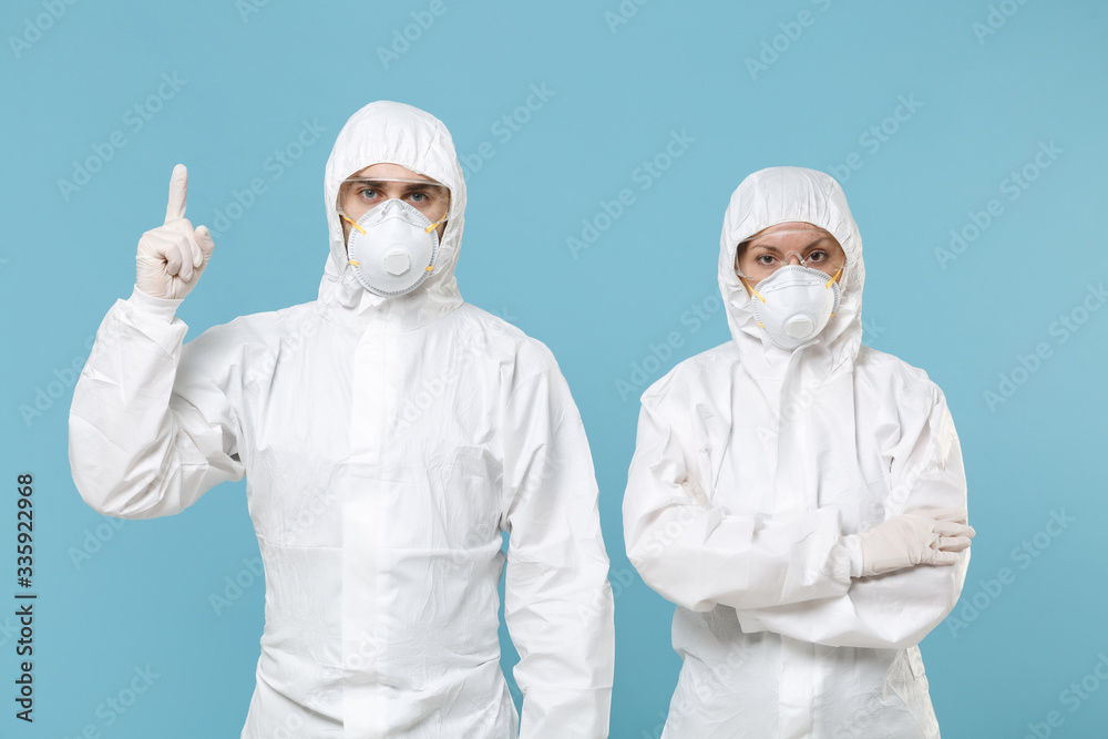 Fototapeta premium People in protective suits respirator masks isolated on blue background studio. Epidemic new rapidly spreading coronavirus 2019-ncov originating in Wuhan China virus concept pointing fingers copyspace