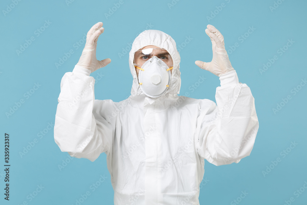 Man in white protective suit respirator mask isolated on blue background studio. Epidemic pandemic new rapidly spreading coronavirus 2019-ncov originating in Wuhan China, medicine flu virus concept. Man in white protective suit respirator mask isolated on blue background studio. Epidemic pandemic new rapidly spreading coronavirus 2019-ncov originating in Wuhan China, medicine flu virus concept.