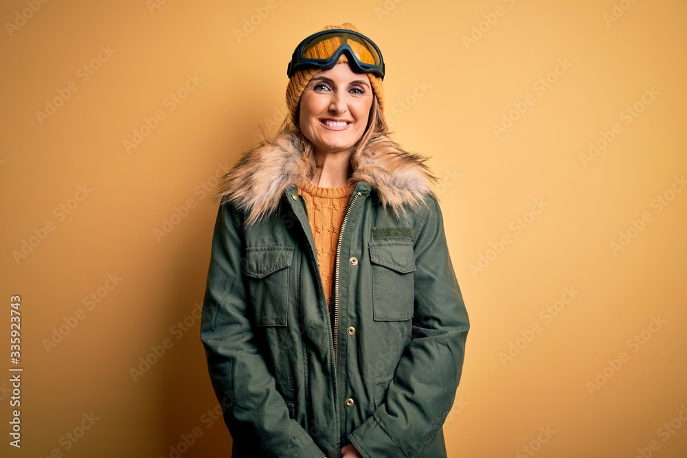 Middle age beautiful blonde skier woman wearing snow sportwear and ski goggles with a happy and cool smile on face. Lucky person.