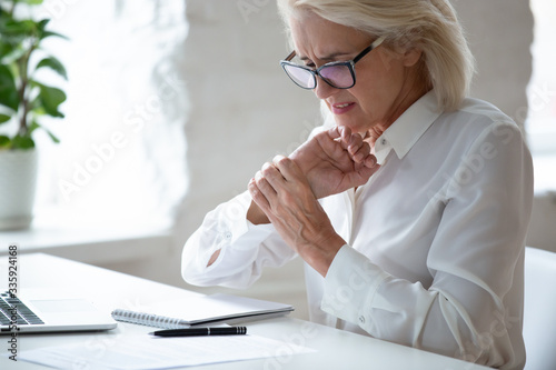 Quadro em tela Unhappy 60 years old businesswoman holding wrist close up, suffering from strong pain in hand