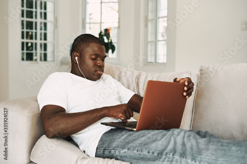 A man of African appearance at home in front of a laptop working on the couch