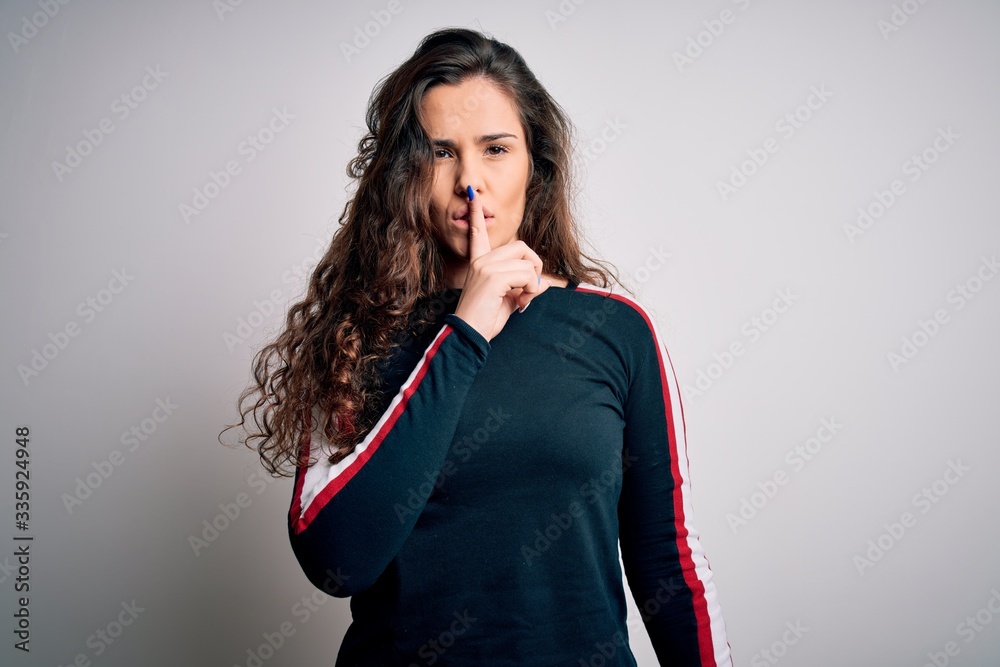 Young beautiful woman with curly hair wearing casual sweater over isolated white background asking to be quiet with finger on lips. Silence and secret concept.