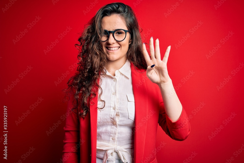 Young beautiful woman with curly hair wearing jacket and glasses over red background showing and pointing up with fingers number four while smiling confident and happy. Young beautiful woman with curly hair wearing jacket and glasses over red background showing and pointing up with fingers number four while smiling confident and happy.