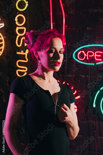 Woman with pink hair and fluorescent make-up in nightclub with neon light.