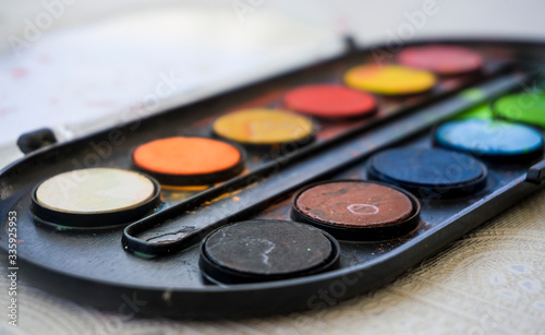 Colors on watercolor palette closeup. Selective focus. Black, blue, brown, red, yellow, green, orange colors on palette.