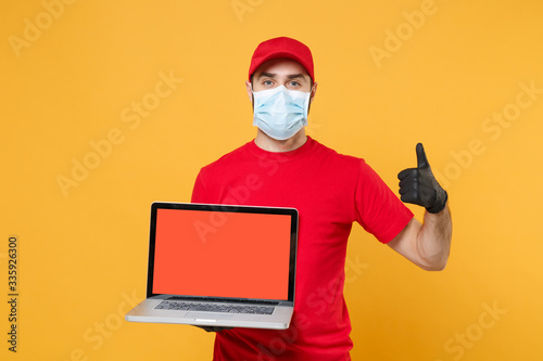 Delivery man in red cap blank t-shirt uniform mask gloves isolated on yellow background studio Guy employee work hold laptop pc computer Service quarantine pandemic coronavirus virus 2019-ncov concept