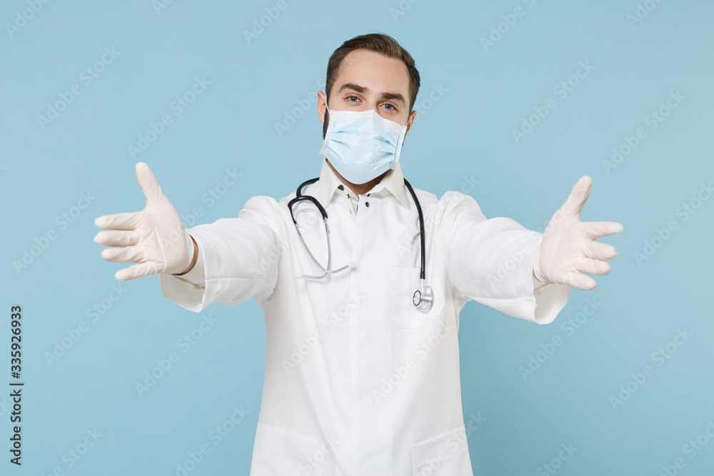 Male doctor man in white medical gown sterile face mask gloves isolated on blue background. Epidemic pandemic coronavirus 2019-ncov sars covid-19 flu virus concept. Standing with outstretched hands. Male doctor man in white medical gown sterile face mask gloves isolated on blue background. Epidemic pandemic coronavirus 2019-ncov sars covid-19 flu virus concept. Standing with outstretched hands.