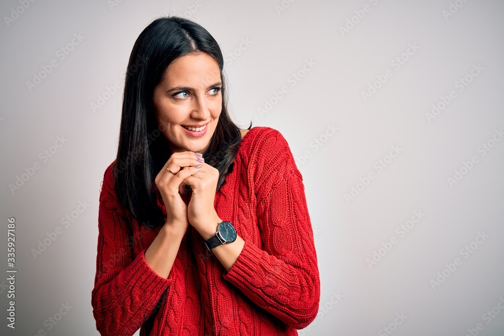 Young brunette woman with blue eyes wearing casual sweater over isolated white background laughing nervous and excited with hands on chin looking to the side Young brunette woman with blue eyes wearing casual sweater over isolated white background laughing nervous and excited with hands on chin looking to the side