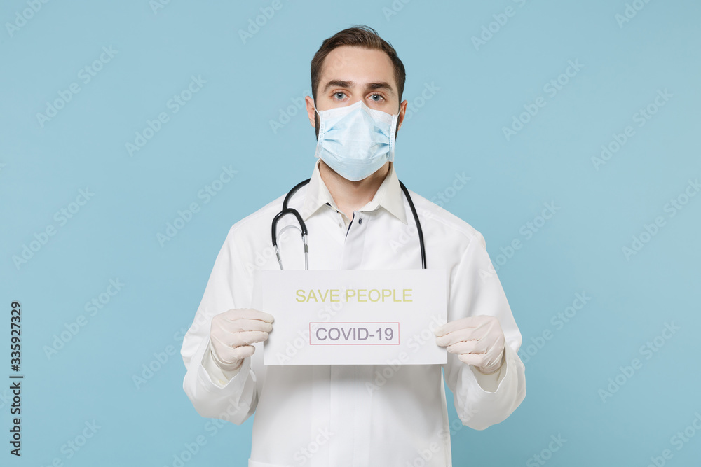 Male doctor man in medical gown face mask gloves isolated on blue background. Epidemic pandemic rapidly spreading coronavirus 2019-ncov sars covid-19 flu virus concept. Hold nameplate save people. Male doctor man in medical gown face mask gloves isolated on blue background. Epidemic pandemic rapidly spreading coronavirus 2019-ncov sars covid-19 flu virus concept. Hold nameplate save people.