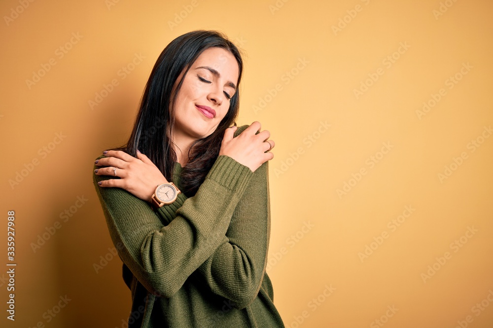 Young brunette woman with blue eyes wearing green casual sweater over yellow background Hugging oneself happy and positive, smiling confident. Self love and self care Young brunette woman with blue eyes wearing green casual sweater over yellow background Hugging oneself happy and positive, smiling confident. Self love and self care