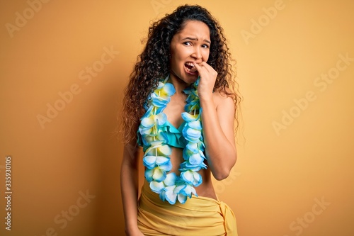 Young beautiful american woman on vacation wearing bikini and hawaiian lei flowers looking stressed and nervous with hands on mouth biting nails. Anxiety problem.