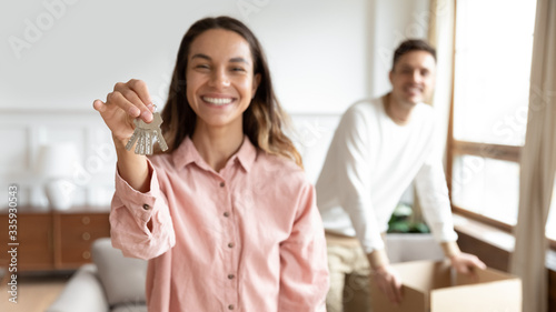 Focus on female hand holding keys from new apartment. Young family couple excited by purchasing new house. Happy clients homeowners satisfied buying real estate, spouses renters moving into flat.