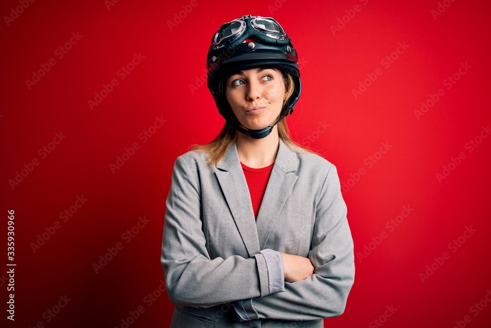 Young beautiful blonde motorcyclist woman wearing motorcycle helmet over red background smiling looking to the side and staring away thinking. Young beautiful blonde motorcyclist woman wearing motorcycle helmet over red background smiling looking to the side and staring away thinking.