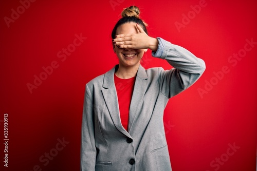 Young beautiful blonde businesswoman with blue eyes wearing glasses and jacket smiling and laughing with hand on face covering eyes for surprise. Blind concept.