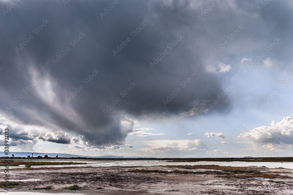 Dark storm cloud bringing rain in South San Francisco bay; Tidal ponds and marsh land visible under the clouds; Don Edwards National Wildlife Refuge, San Jose, California