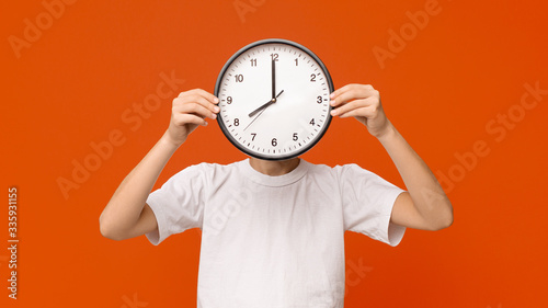 Teen boy covering his face with big clock, orange panorama photo