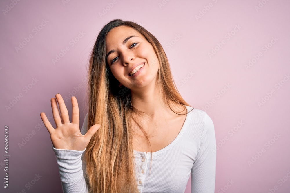 Young beautiful blonde woman with blue eyes wearing white t-shirt over pink background showing and pointing up with fingers number five while smiling confident and happy. Young beautiful blonde woman with blue eyes wearing white t-shirt over pink background showing and pointing up with fingers number five while smiling confident and happy.