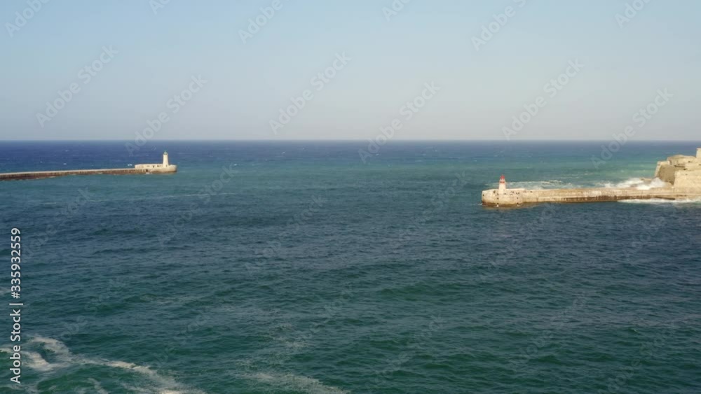 Aerial view of Grand harbor - main port of Malta island. Red lighthouse, fort Ricasoli. Big waves in mediterranean sea.