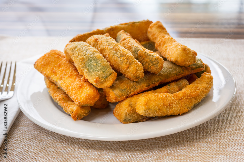 A view of a plate of deep fried zucchini sticks, in a restaurant or kitchen setting. A view of a plate of deep fried zucchini sticks, in a restaurant or kitchen setting.