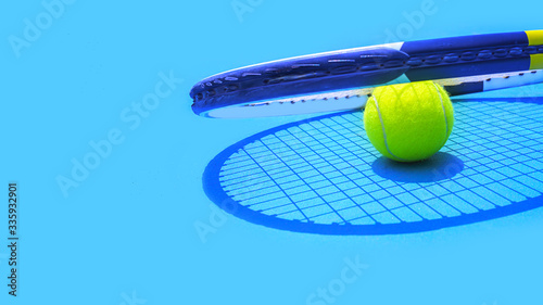 Summer sport concept with tennis ball and racket on blue hard tennis court.