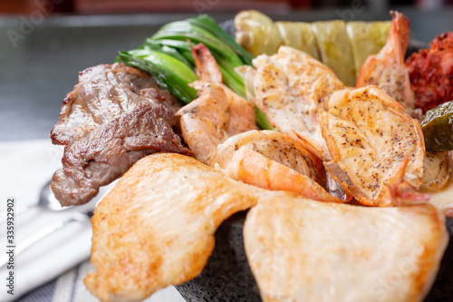 A view of a meat platter in a molcajete bowl, featuring chicken, steak, and shrimp, in a restaurant or kitchen setting.