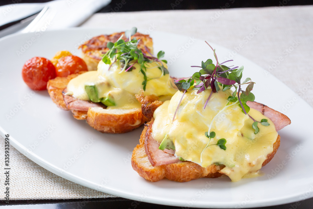 A view of a plate of Eggs Benedict, in a restaurant or kitchen setting. A view of a plate of Eggs Benedict, in a restaurant or kitchen setting.