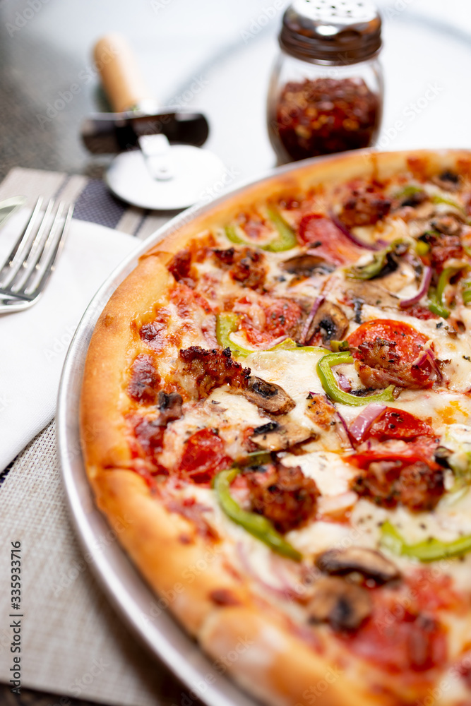 A view of a rustic meat and veggie pizza pie, in a restaurant or kitchen setting.
