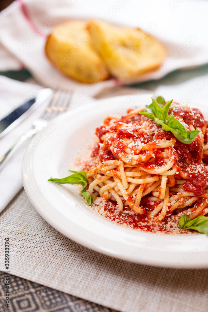 A view of a dish of spaghetti with marinara sauce and side of garlic bread, in a restaurant or kitchen setting.