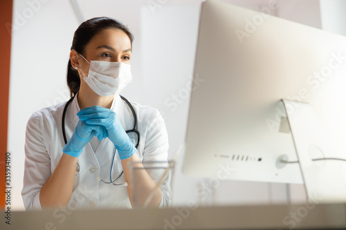 Beautiful doctor in medical mask doing tasks at laptop photo