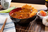 A bowl of Japanese curry with katsu chicken, in a restaurant or kitchen setting.